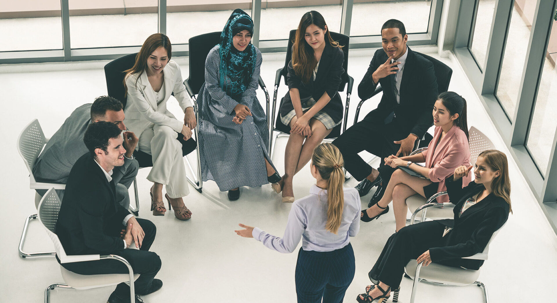 Eight diverse professionals seated in a semicircle around one speaker in business attire.