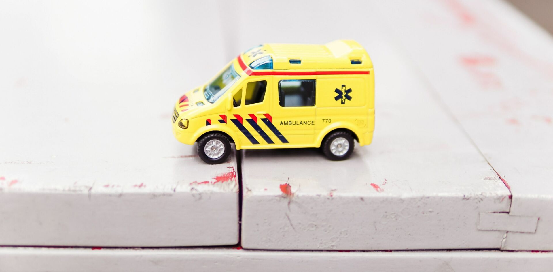 Yellow toy EMT vehicle on white wooden tabletop.