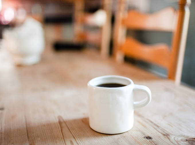 focus on white ceramic mug with out of focus wooden table top and chairs in the background.