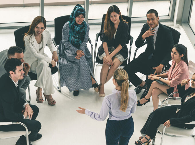 Eight diverse professionals seated in a semicircle around one speaker in business attire.