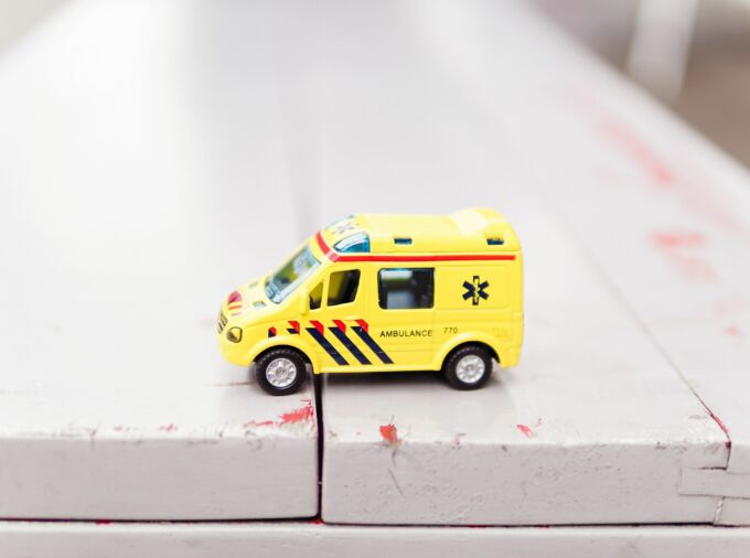Yellow toy EMT vehicle on white wooden tabletop.
